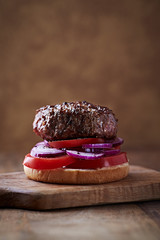Tasty humburger with tomatoes and red onion. Brown wooden background. 
