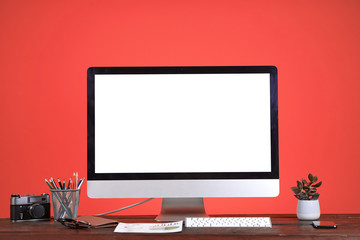 Workplace concept with blank white computer screen at wooden desk over coral background, copy space