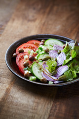 Healthy salad with tomatoes, cucumber, lettuce, olives and capers on rustic wooden background. 