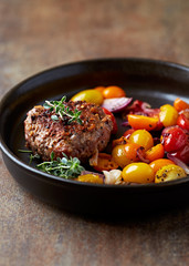 Fried hamburger steak with various cherry tomatoes and fresh herbs. Rustic background. 