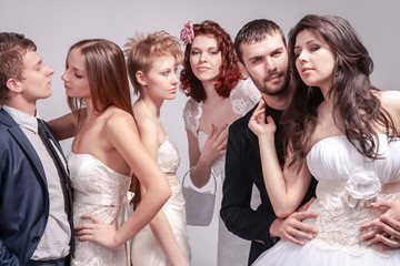 Portrait of Five Loving Caucasian People Posing in Wedding Clothing Together in One Group. Against Gray Background Indoors.
