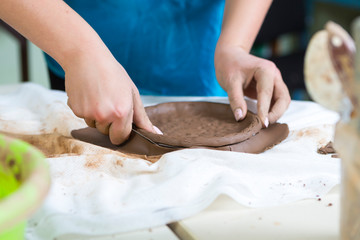 Pottering Concepts. Closeup of Hands of Female Worker Cutting A plate of Wet Clay on Table Before Moulding.