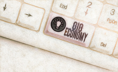 Text sign showing Gig Economy. Business photo showcasing free market system in which temporary positions are common White pc keyboard with empty note paper above white background key copy space