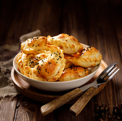 Baked dumplings (pierogi) with mushroom stuffing in a ceramic bowl on a wooden table, close-up. ...