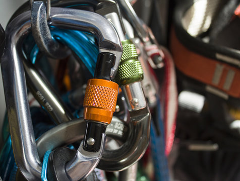 A set of screwgate carabiners on a rock climbing rack, with slings, quickdraws and harnesses on the background