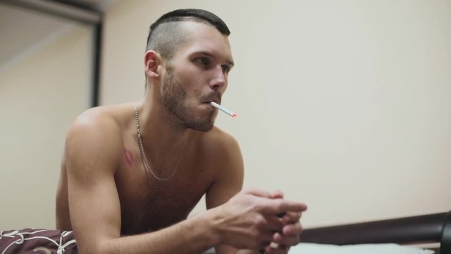 Close up serious topless good-looking fit young man smoking cigarette in bed at home bedroom tobacco guy handsome apartment slow motion