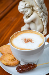 A delicious coffee break cappuccino, served with cookies and sugar sticks in a white cup on a wooden table.