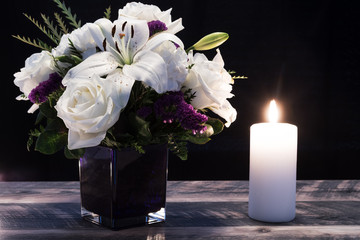 Bouquet of white flowers in a purple vase, white candle on a wooden boards. Vintage home decor dark...