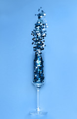 Trendy blue heart-shaped confetti poured out of champagne glass. Love and celebration concept. Color of the year 2020 concept. Flat lay.