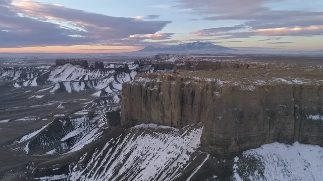 Aerial view rotating around viewpoint with vehicles on top of cliff in the desert during winter with snow below in Utah.