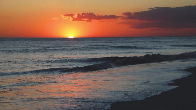 A beautiful full sunset over breaking ocean waves on Gulf of Mexico Florida beach on a vacation by the sea is featured in this one minute long video footage