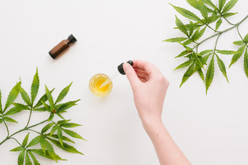 Woman's hand, glass bottles with CBD oil, THC tincture and hemp leaves on a white background. Flat lay, minimalism. Cosmetics CBD oil.