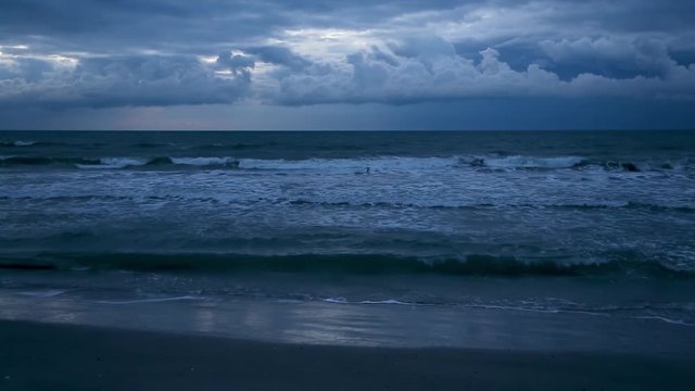 Looping video features a moody blue ocean beach with waves with crashing surf under a cloudy early morning sky