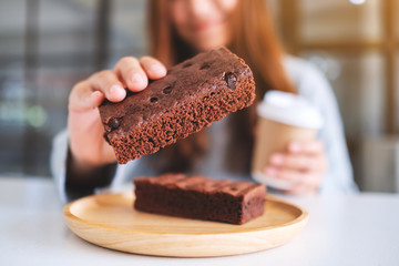 Closeup image of a beautiful woman holding and eating a piece of brownie cake while drinking coffee