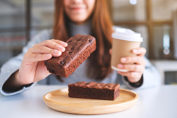 Closeup image of a beautiful woman holding and eating a piece of brownie cake while drinking coffee