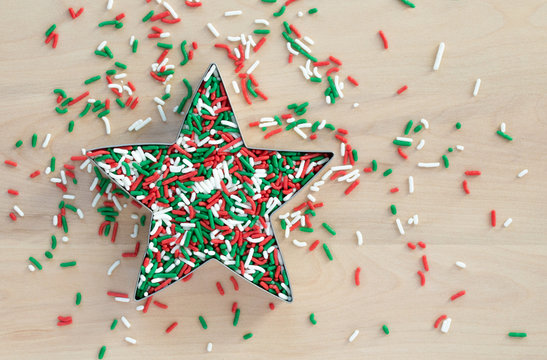 cookie cutter shaped like a Christmas star filled with red, green and white candy sprinkles on a wood background with copy space