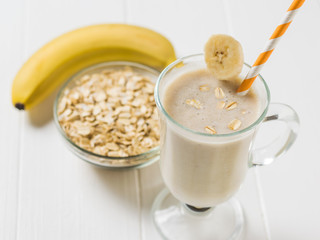The orange straw in the glass with banana oatmeal smoothies on a white table. Vegetarian smoothie.
