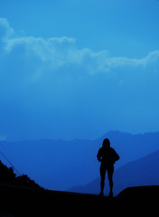 Obraz premium Young tourist woman standing on top of mountain and looking at a beautiful landscape. girl tourist relax on hill in summer epic sky up view. High peak tour Classic blue pantone color year 2020 concept