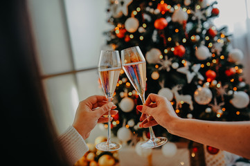 two cheers glasses with champagne against the background of the Christmas tree in female hands