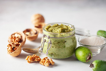 Feijoa jam with sugar and walnut in a jar on a light background. Iodine product