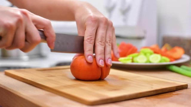 Woman using kitchen knife is cutting fresh persimmon on wooden board