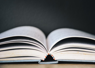 An old book open on wooden table with black color wall background and light frome above, copy space