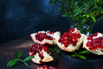 Fresh ripe pomegranate is divided into pieces and lies on a dark table. Horizontal photo.