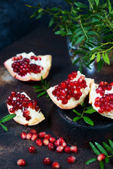 Close up Fresh ripe pomegranate is divided into pieces and lies on a dark table. Vertical photo.