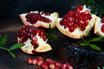 Close Fresh ripe pomegranate with drops of water is divided into pieces and lies on a dark table. Horizontal photo.