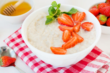 Close up healthy balanced Breakfast of oatmeal with strawberries and honey on a white background. Horizontal photo.