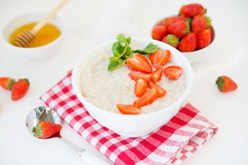 Healthy balanced Breakfast of oatmeal with strawberries and honey on a white background. Horizontal photo