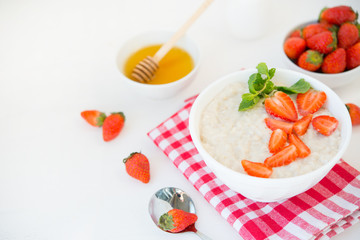 Healthy balanced Breakfast of oatmeal with strawberries and honey on a white background. Horizontal photo with copy space.