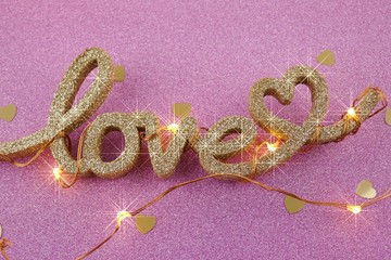 Love concept. Valentine's Day. The word love and a shining garland on a pink glitter background.Romantic twinkle background.