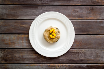 Cat's birthday concept. Pet feed with festive candle in shape of three on dark wooden background top-down