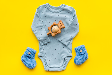 Cute baby clothes - suit - booties and accessories on yellow table top-down