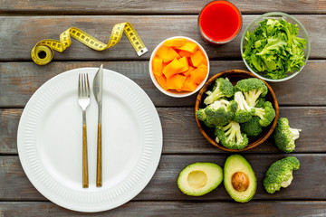 Diet program concept. Empty plate, measure tape and vegetables on dark wooden background top view