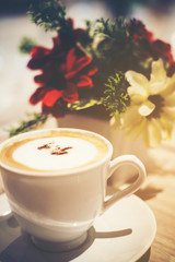 Cappuccino coffee placed on a wooden table and blurred floral background.