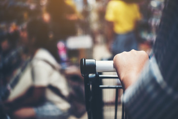 Asian woman's hand with supermarket, trolley and many objects that are blurred background.