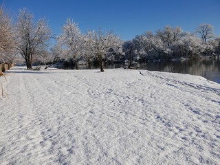 Wide scenic tranquil view of fresh white snow covering the ground by the pond