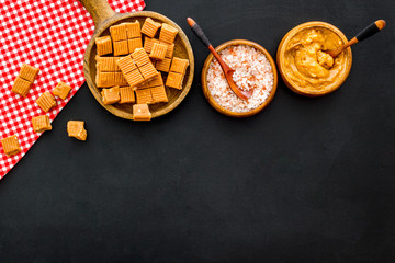 Prepare salted caramel. Scoop with sweet cubes, melted caramel and salt on black background top view copy space