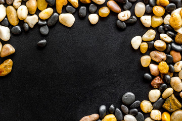 Summer trip to sea concept. Stones on black background top-down frame copy space