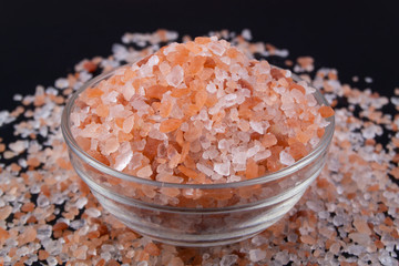 Fototapeta na wymiar Pink rock salt in bowl on black background close-up