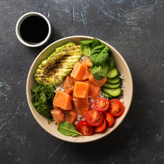 Organic poke bowl with salmon, avocado and vegetables on dark background