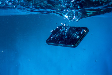 black and white phone dropped into the water. phone in water. blue water. phone in water...