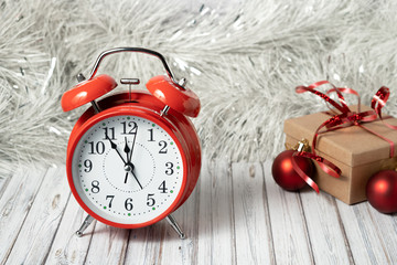 Red vintage alarm clock and gift box on a wooden table decorated with a garland and red Christmas balls for the New Year or XMAS. Mail, courier or delivery service concept. Copy space
