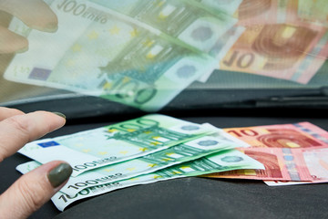 Euro banknotes in the woman hand near dashboard and their reflection in the windshield inside of a car