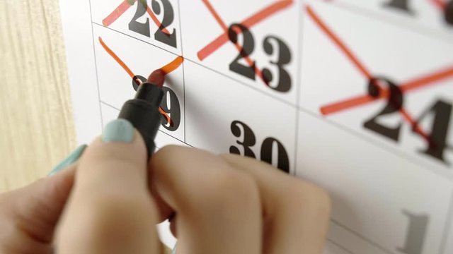 Female hand crosses with red marker the calendar day 29. Slow motion shot. Close up