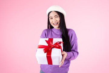 Happy Asian woman wearhing purple sweater holding gift box on pink background.