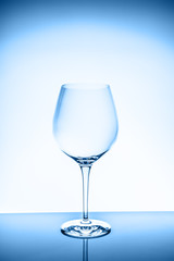 Red wine glass on the light background. Fine cristal glassware concept. Vertical, toned in blue