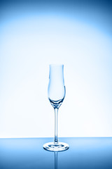 Liqueur glass on the light background. Fine cristal glassware concept. Vertical toned in blue